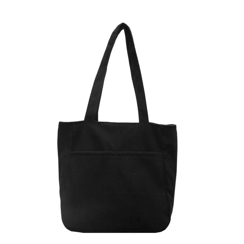 Black corduroy tote bag with long handles and front pocket on white background