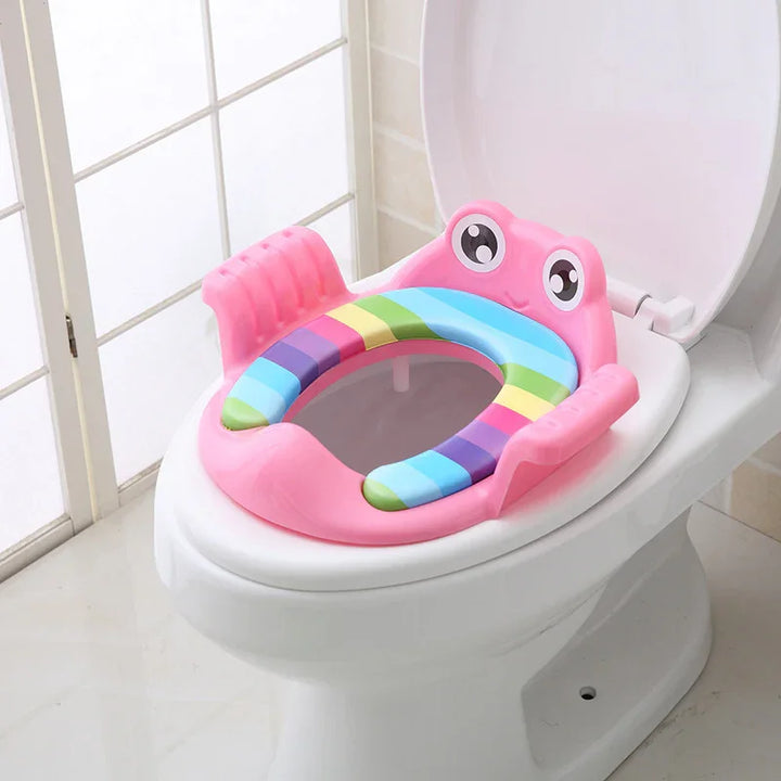 Pink frog-shaped padded children's potty training seat with rainbow cushion on white toilet