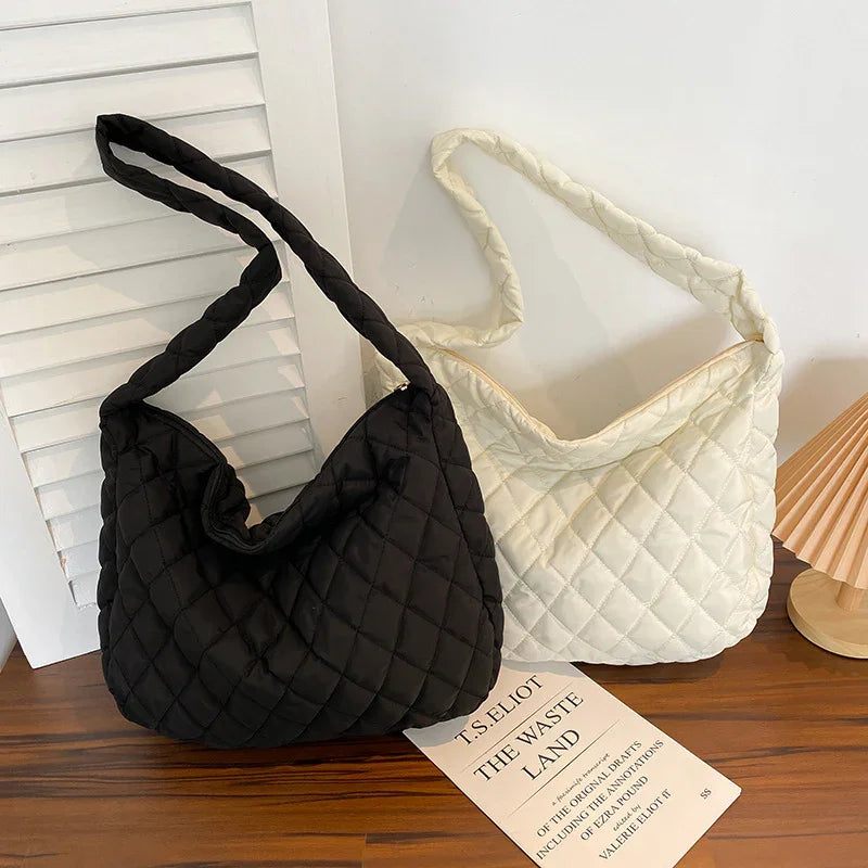 Black and white quilted shoulder bags on wooden surface with T.S. Eliot book and lamp