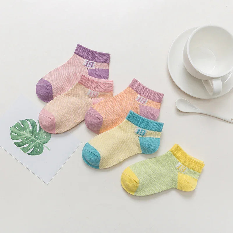 Set of five colorful ankle socks with number 19 in pastel purple, pink, orange, blue, and yellow shades on white surface with cup and saucer