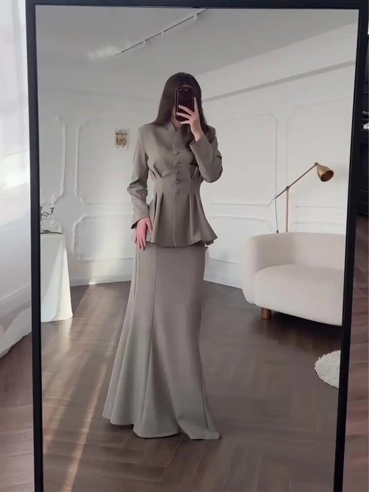 Woman in taupe buttoned peplum blazer and matching long skirt taking mirror selfie in elegant room