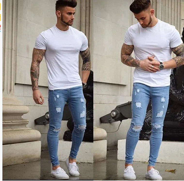 Man wearing a fitted white t-shirt and ripped skinny blue jeans with white sneakers, posing outdoors