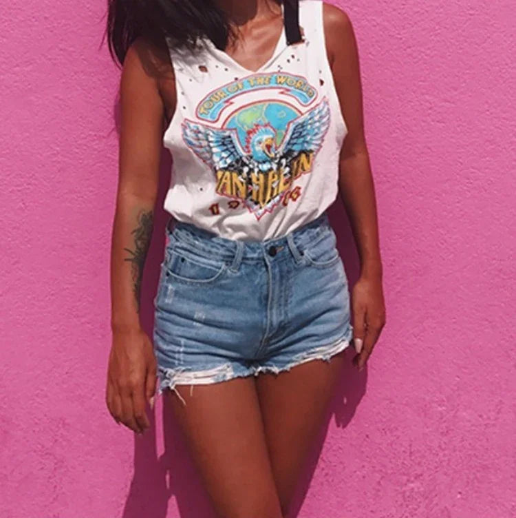 Woman wearing white vintage graphic tank top and ripped denim shorts against pink wall