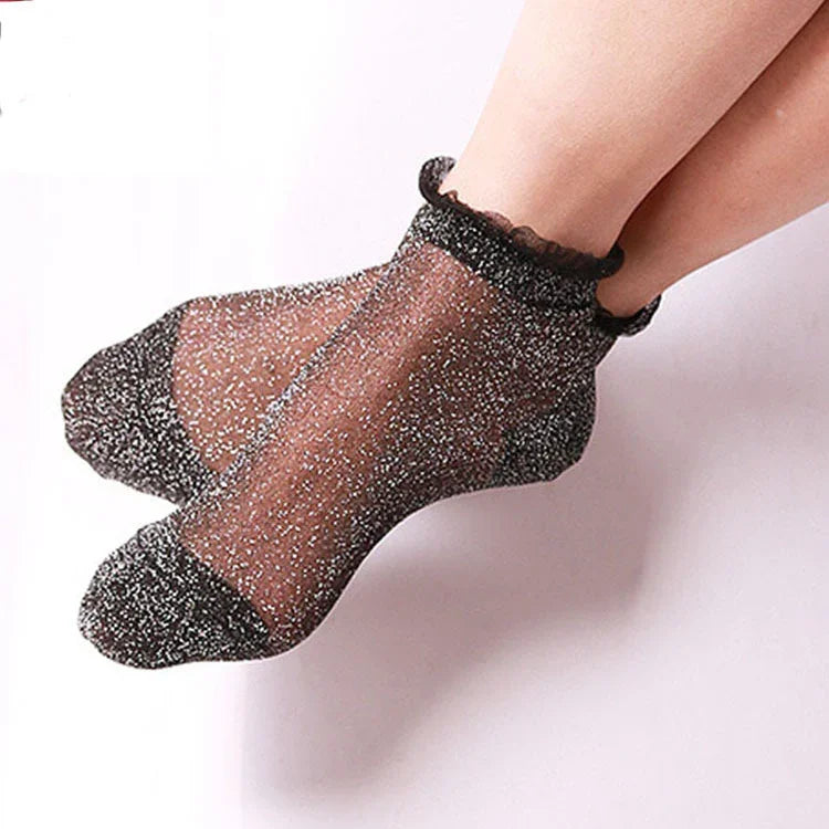 Pair of sheer black ankle socks with silver glitter and ruffled cuffs on feet