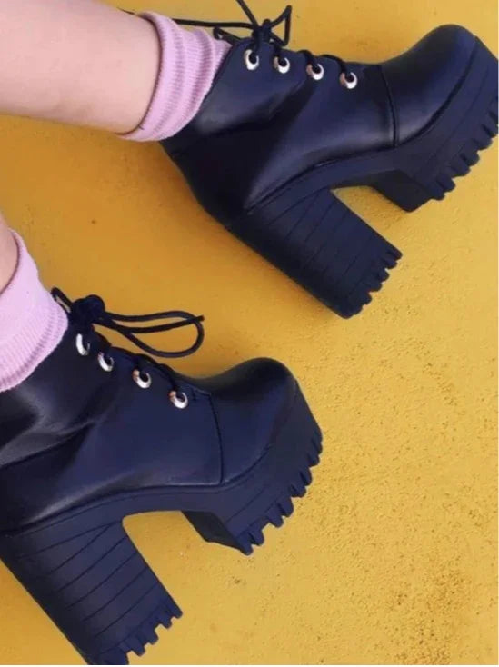 Black chunky platform ankle boots with laces worn with pink socks on yellow floor