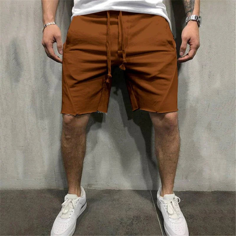 Man wearing rust brown casual shorts with drawstring and white sneakers against gray wall