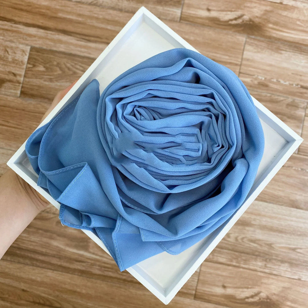 Hand holding white tray with neatly rolled light blue fabric on wooden floor background