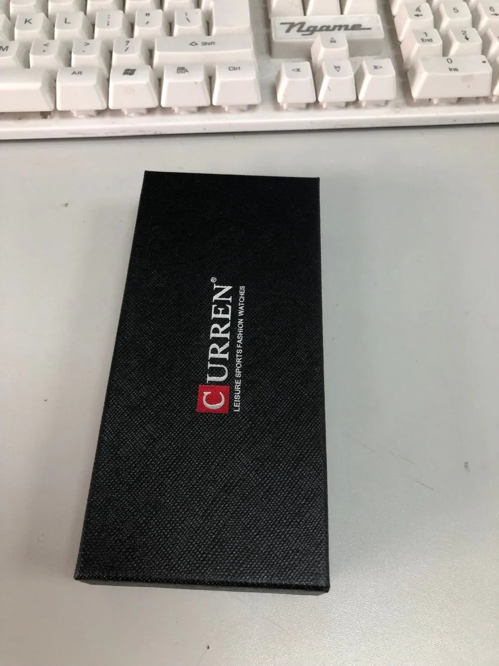Black CURRREN watch box with leisure sports fashion watches text on a white desk near a white computer keyboard