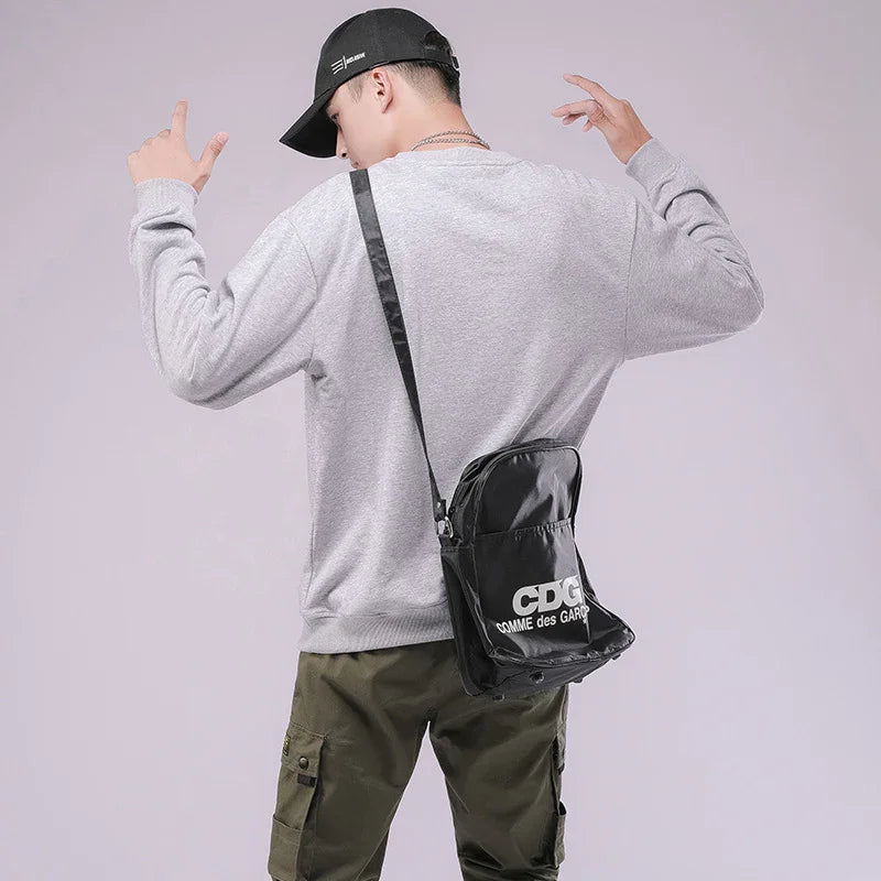 Man wearing gray sweatshirt, olive cargo pants, black cap, and black CDG Comme des Garçons shoulder bag