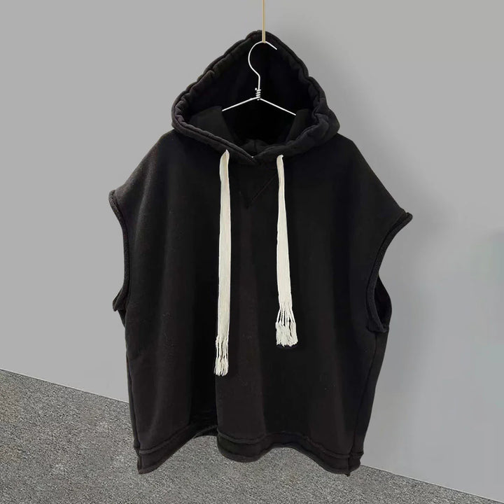 Black sleeveless hoodie with white drawstrings hanging on a wall hook against gray background