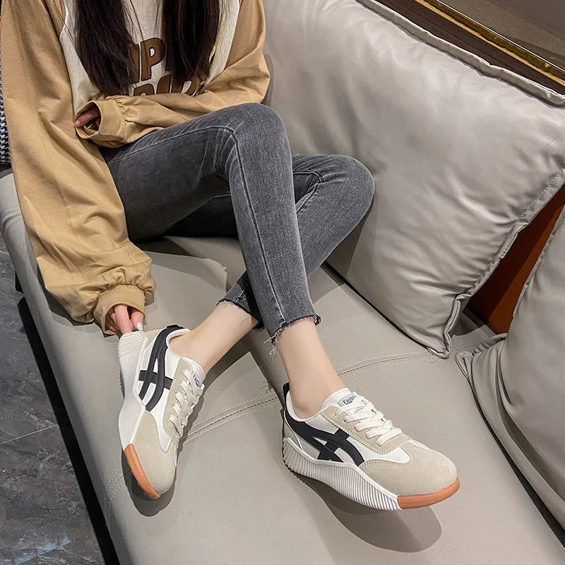 Casual sneakers with beige, black, and white design worn by person sitting on gray couch