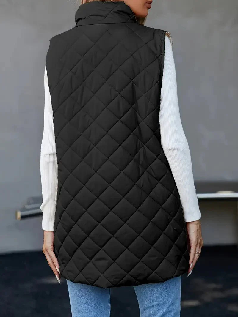 Woman wearing black quilted sleeveless vest over white long-sleeve top and blue jeans from back