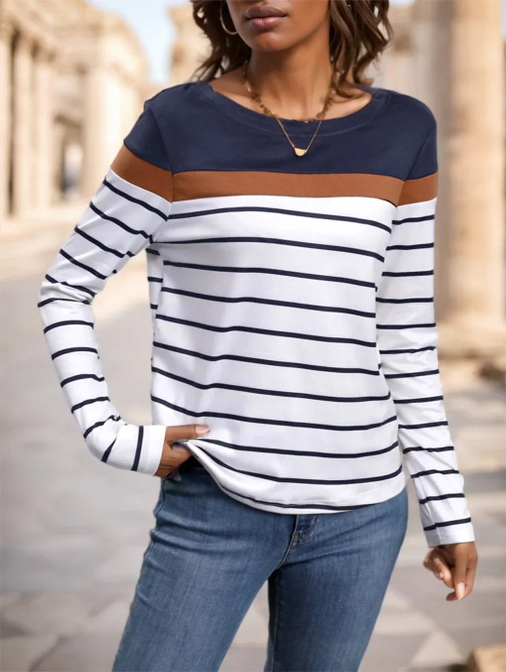 Woman wearing navy, brown, and white striped long sleeve top paired with blue jeans in an outdoor urban setting