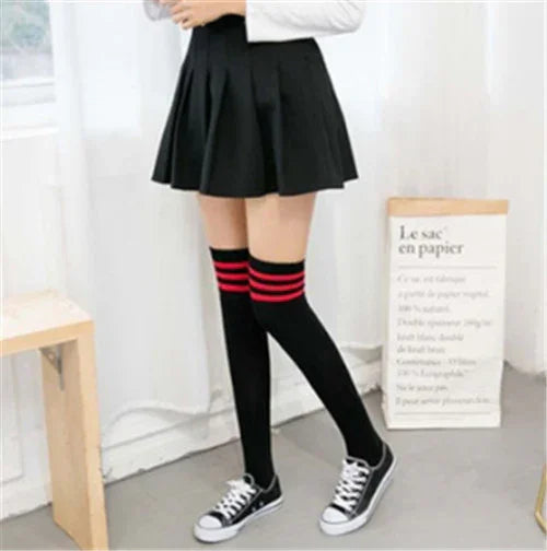 Person wearing black pleated mini skirt, black knee-high socks with red stripes, and black sneakers in bright room