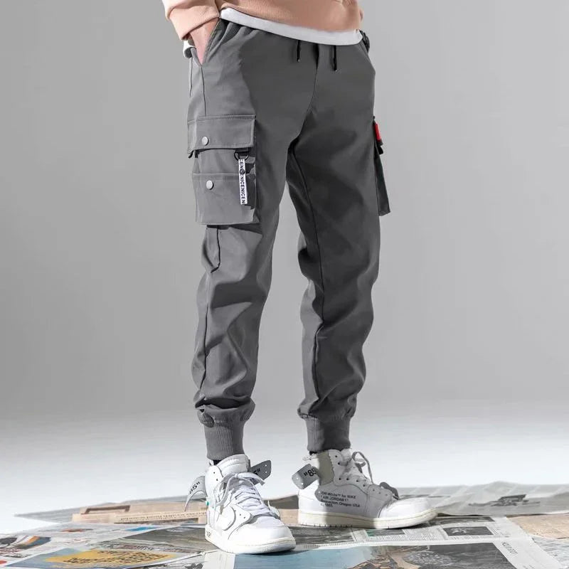 Men's grey cargo jogger pants with multiple pockets styled with white high-top sneakers
