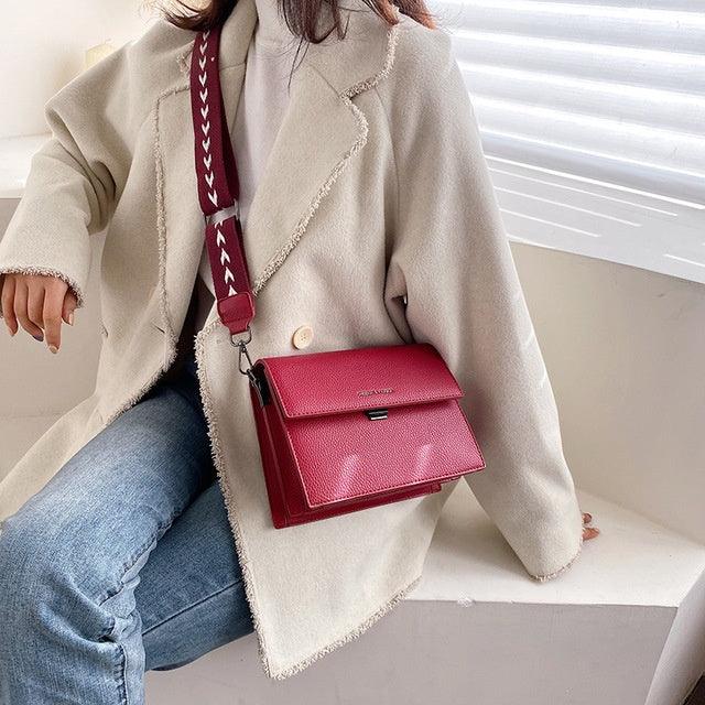 Woman wearing beige coat and blue jeans with a red leather crossbody bag featuring a patterned strap