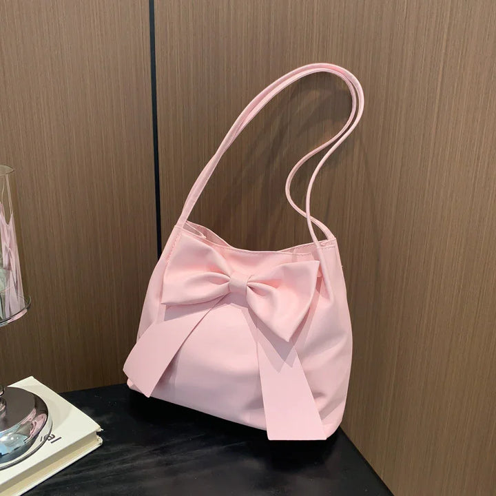 Pink shoulder bag with large bow detail on black surface against wooden wall