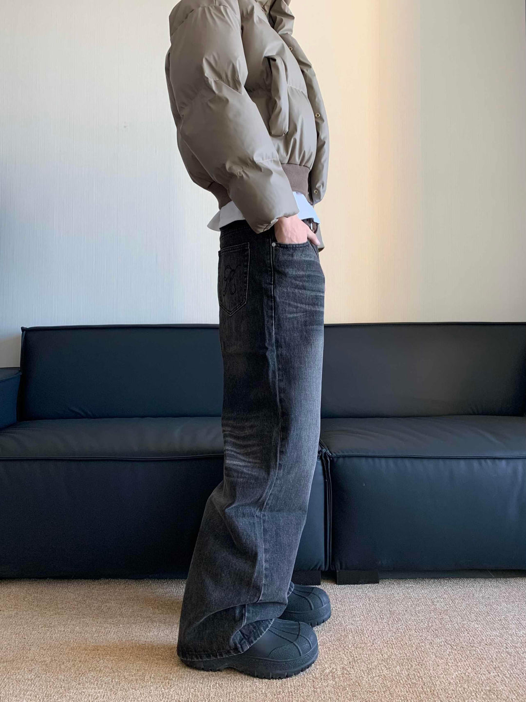 Person wearing beige puffer jacket, baggy black jeans with back pocket detail, and black chunky shoes indoors