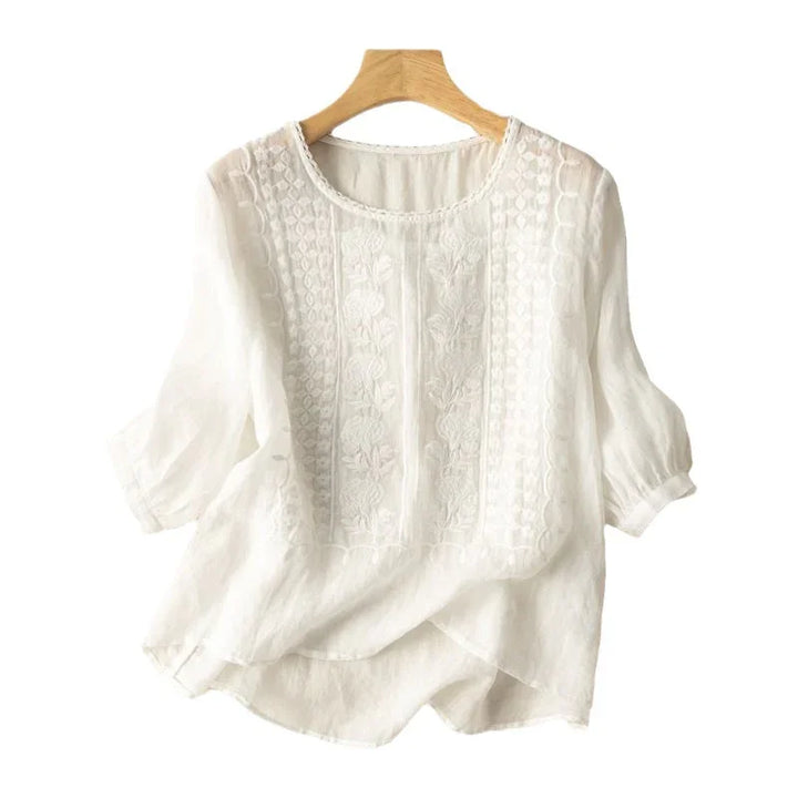 white semi-sheer embroidered blouse with puff sleeves on wooden hanger