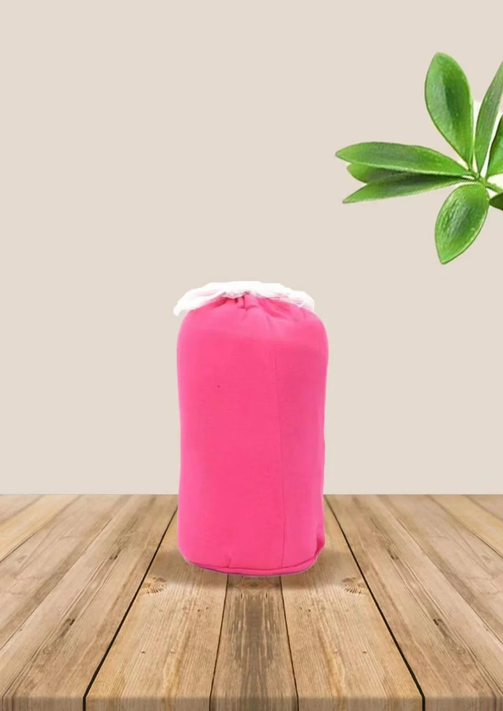 Bright pink fabric pouch with white drawstring on wooden table, green leaves background