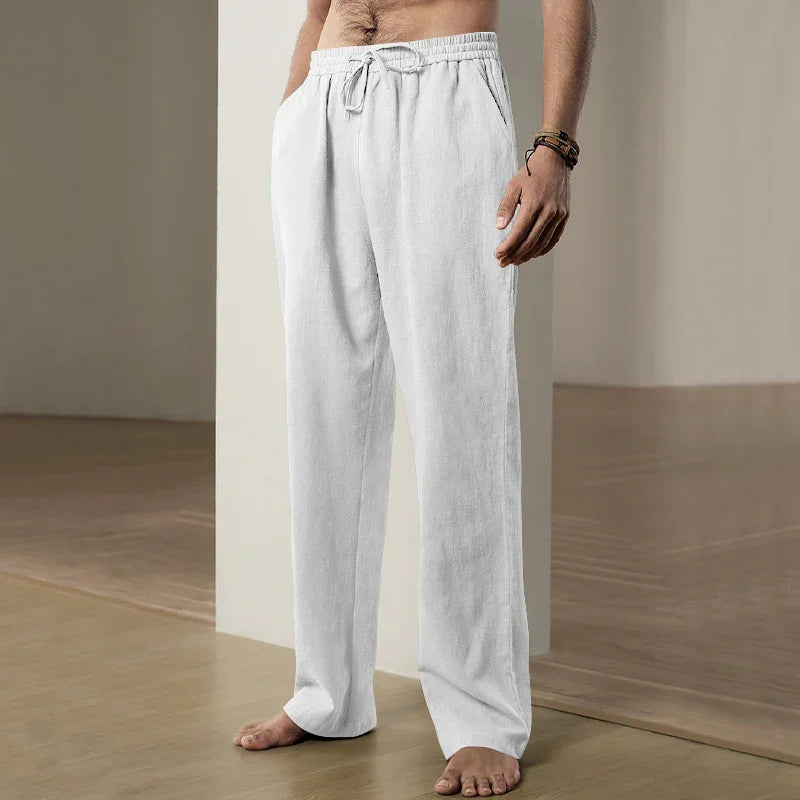 Man wearing white loose-fit drawstring casual pants standing barefoot on wooden floor indoors