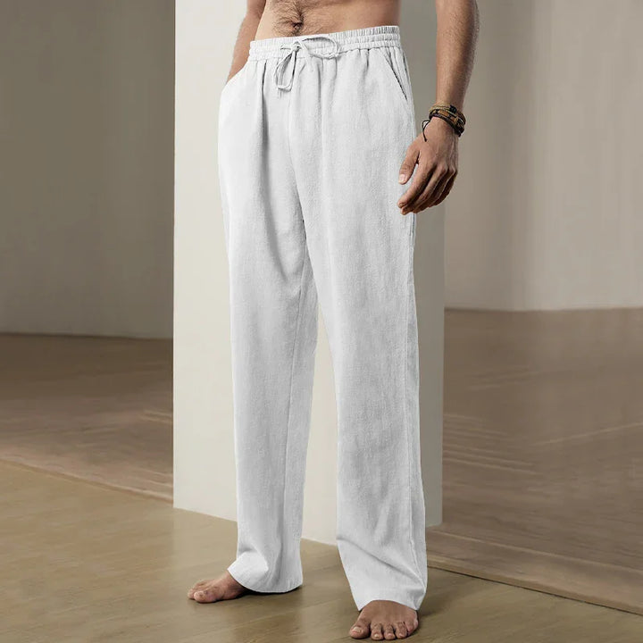 Man wearing white loose-fit drawstring casual pants standing barefoot on wooden floor indoors