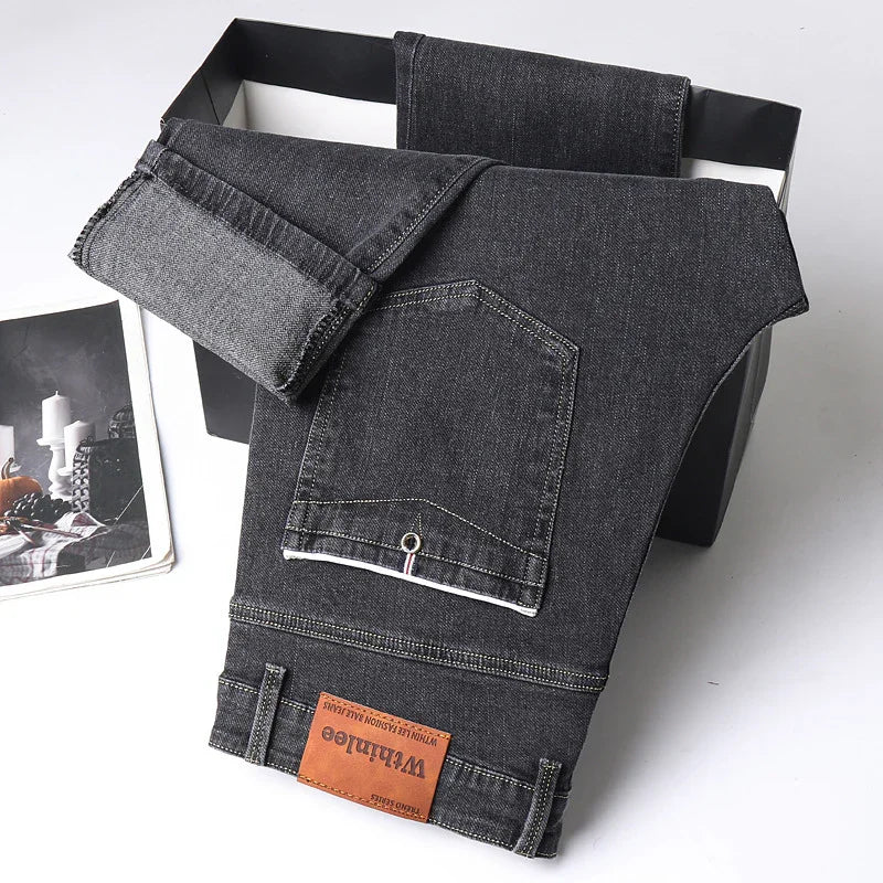 Folded dark gray denim jeans with a leather Whithloe brand patch on a black box