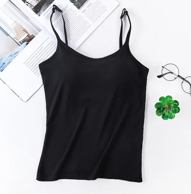 Black spaghetti strap tank top laid flat on white surface with open magazine, round glasses, and small green succulent