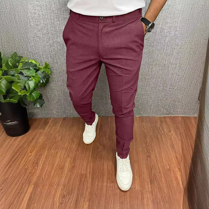 Man wearing slim fit maroon trousers with white sneakers standing on wooden floor