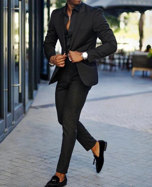 man in slim-fit black suit and black loafers walking on city sidewalk