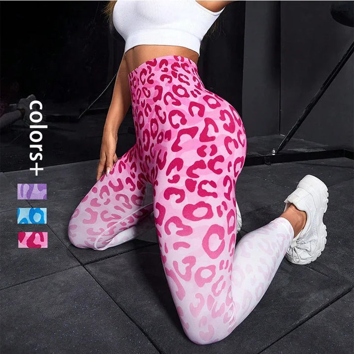 Woman wearing pink ombre leopard print high-waisted leggings and white crop top kneeling on gym floor