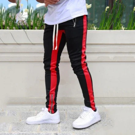 Man wearing black jogger pants with red side stripes and white sneakers outdoors