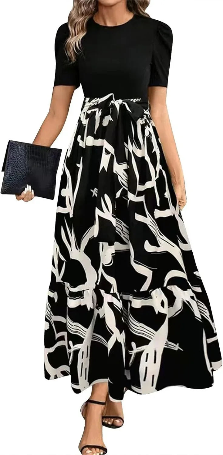 Woman wearing black top with short sleeves and black-and-white abstract print maxi skirt with bow belt, holding black clutch