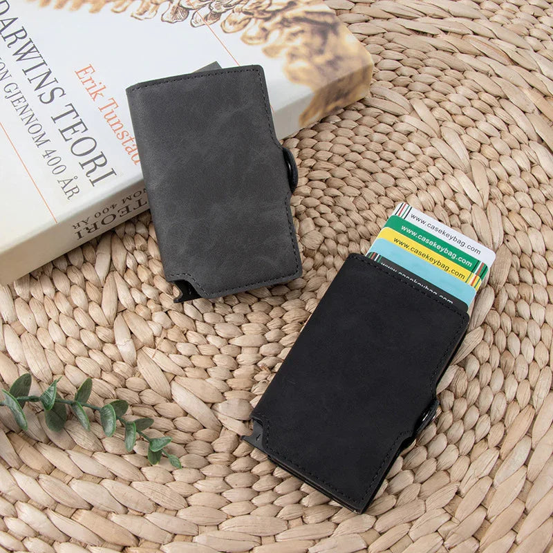 Two minimalist black and gray leather cardholder wallets on woven mat with cards and a book