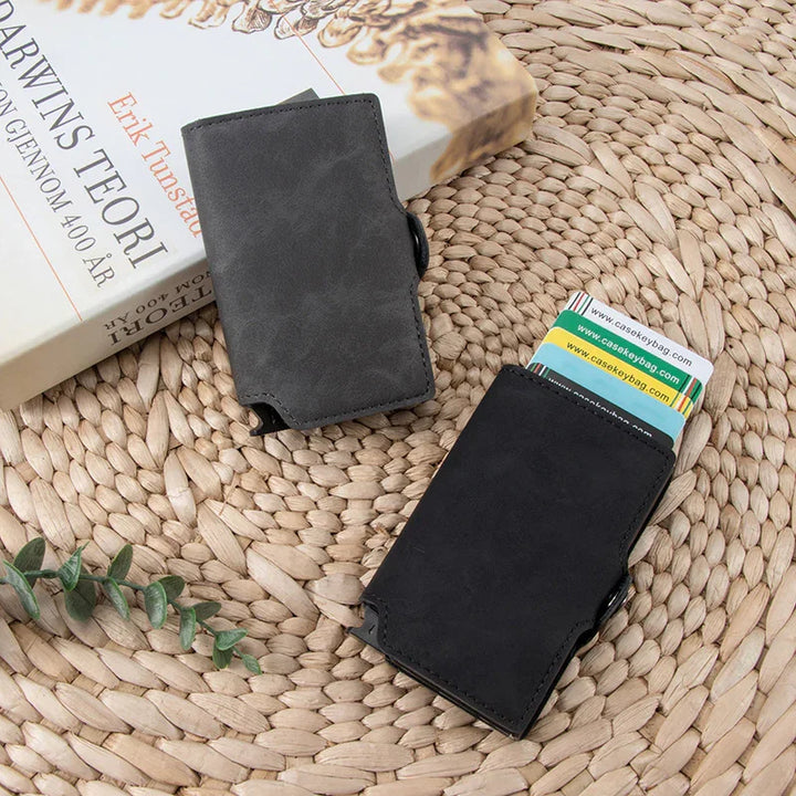 Two minimalist black and gray leather cardholder wallets on woven mat with cards and a book