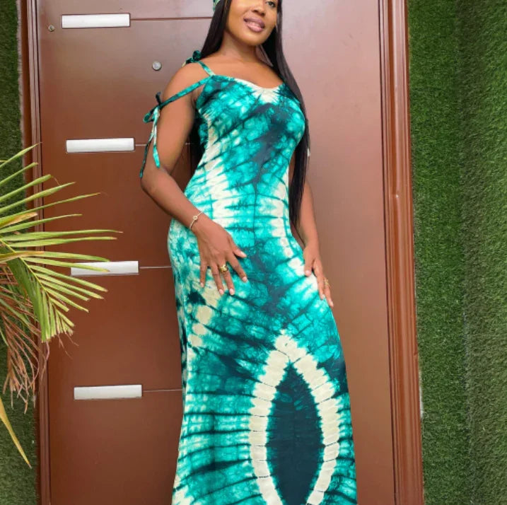 woman wearing teal and white tie-dye maxi dress standing by brown door with green plant nearby