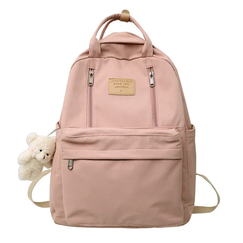 Pink backpack with front zipper pockets and attached small white teddy bear keychain