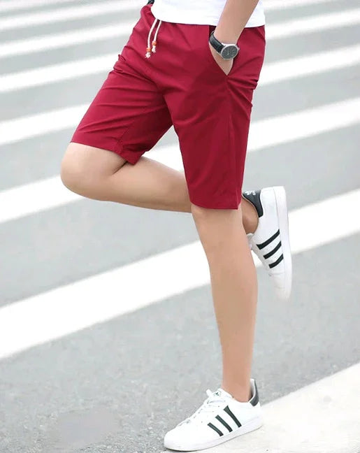 Man wearing red shorts and white sneakers with black stripes standing on a crosswalk