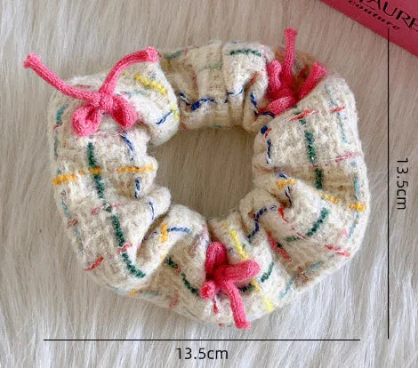 Soft fabric scrunchie with colorful woven plaid pattern and pink drawstring bows on white background