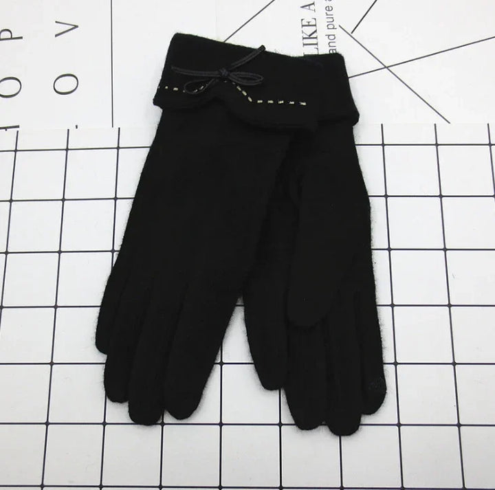 Pair of black winter gloves with wrist bows and stitching detail on a white grid background