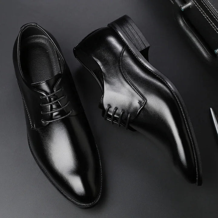 Pair of shiny black leather formal dress shoes with lace-up design on a black surface