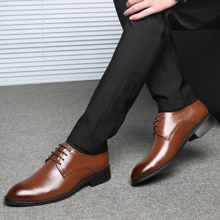 Brown leather men's dress shoes paired with black formal trousers on a gray carpet