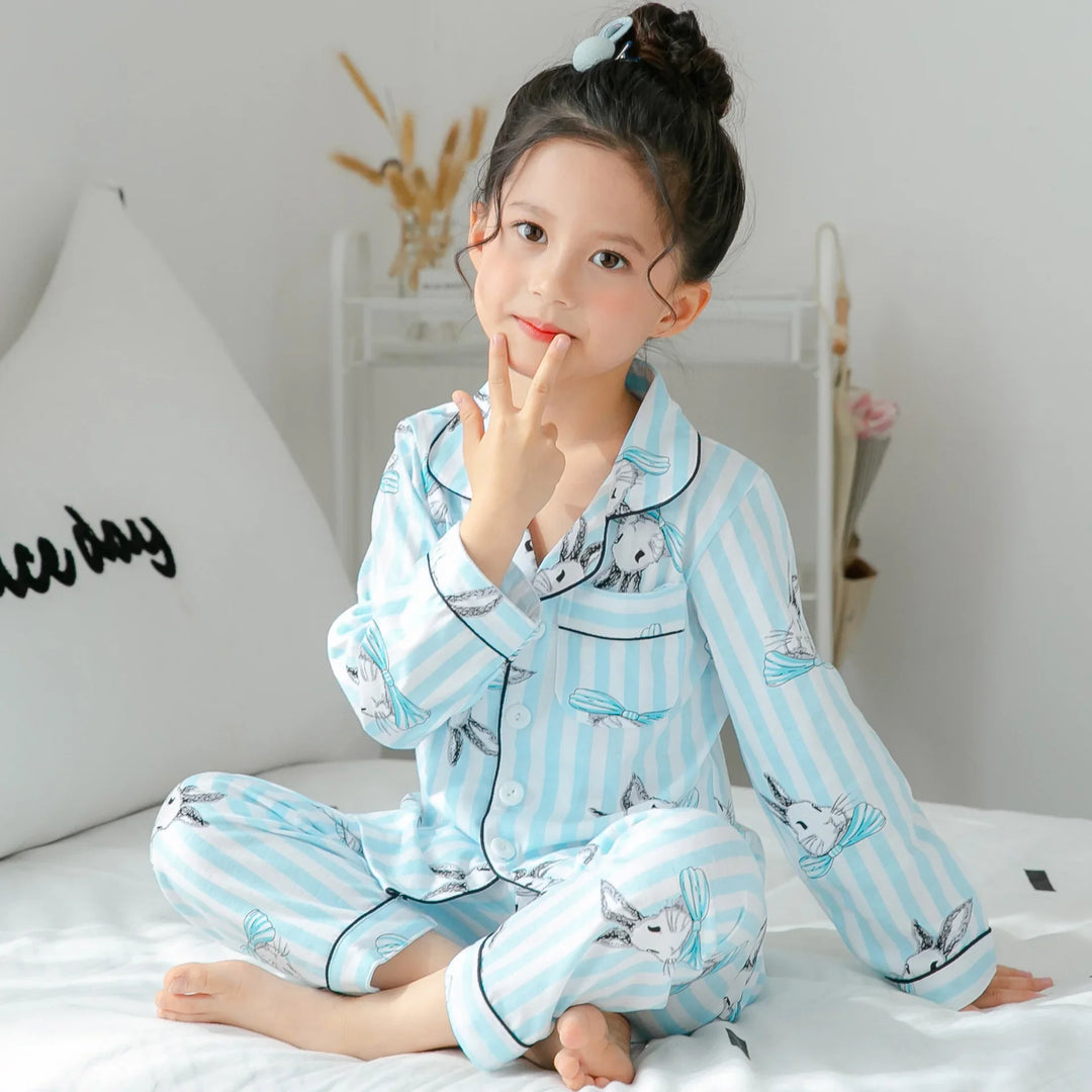 Young girl sitting on bed wearing blue striped bunny print pajamas with hair in a bun
