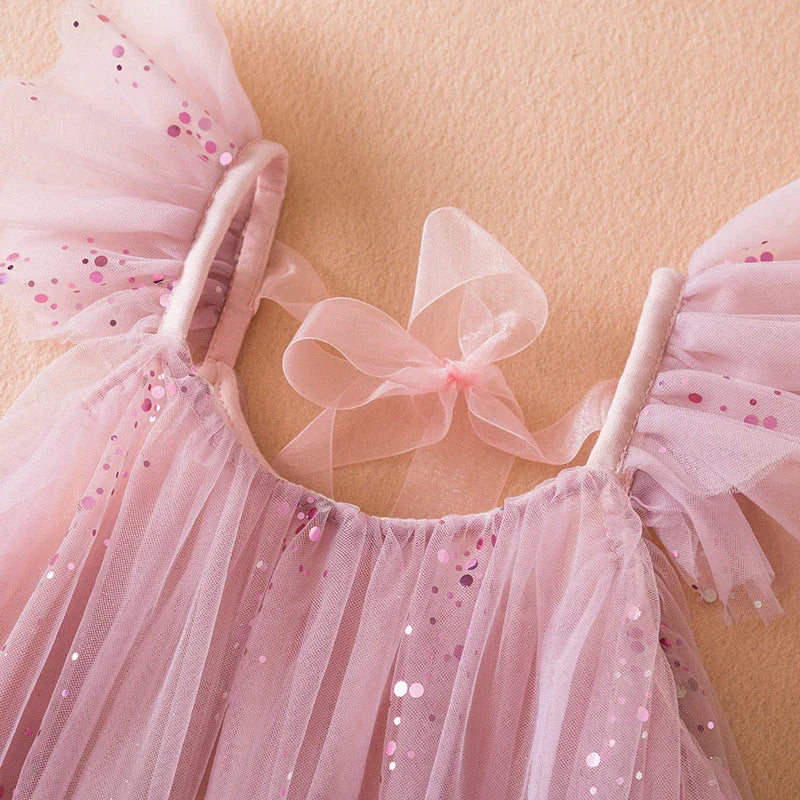 Pink toddler dress with glittery tulle fabric and sheer ribbon bow on beige background