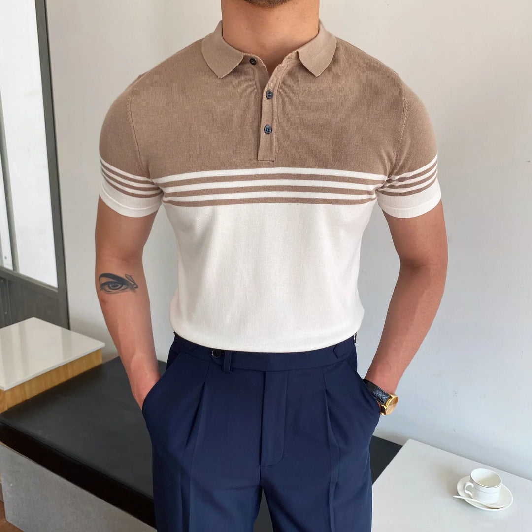 Man wearing beige and white striped short sleeve polo shirt with navy pleated pants indoors
