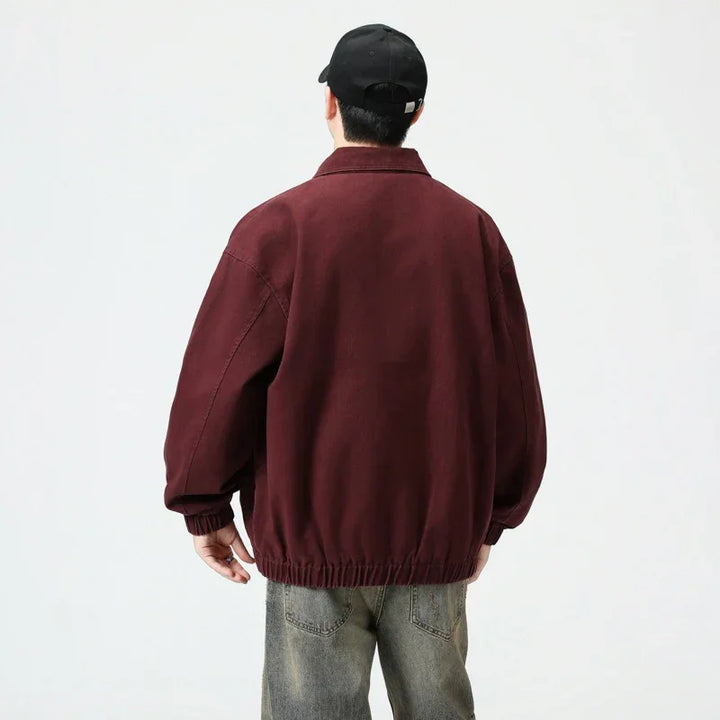 Man wearing oversized maroon jacket and black cap, viewed from the back, against white background