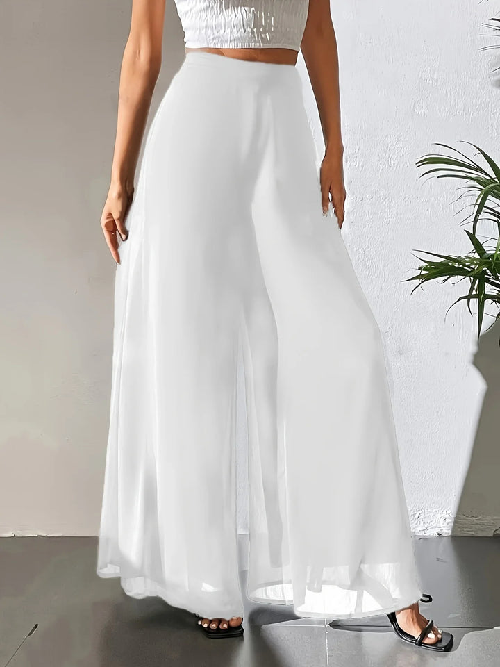 Woman wearing white wide-leg palazzo pants and black open-toe heels against white wall