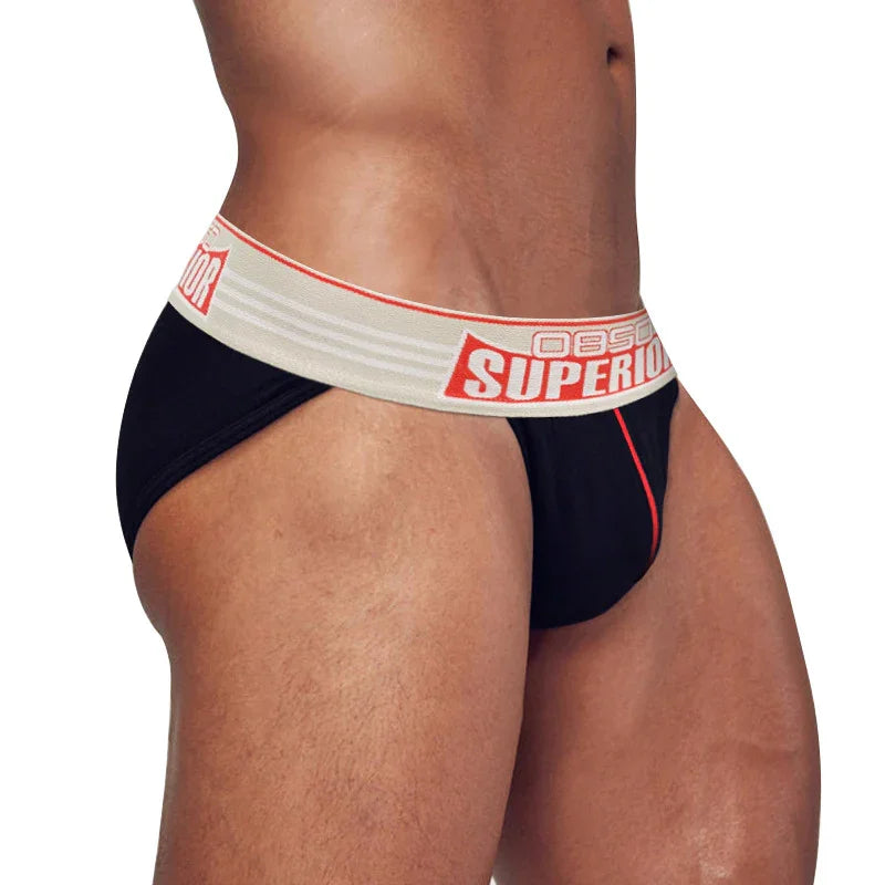 Male model wearing black jockstrap with beige waistband and red vertical stripe on white background
