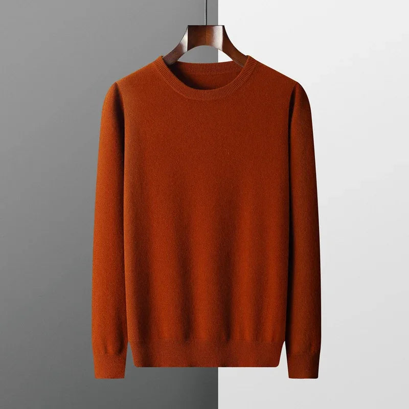 Rust-colored long sleeve crewneck sweater hanging on wooden hanger against gray and white split background