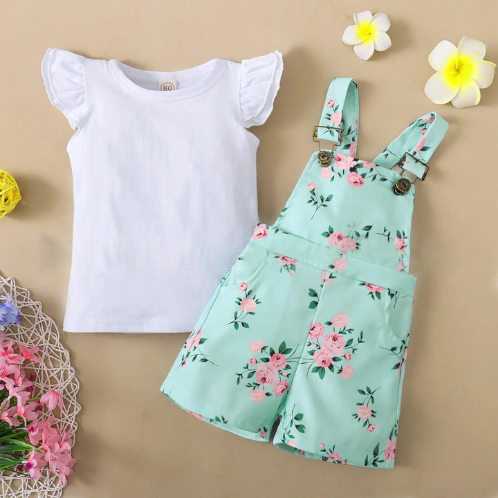 Toddler girl outfit with white flutter sleeve top and mint green floral print overalls on beige background
